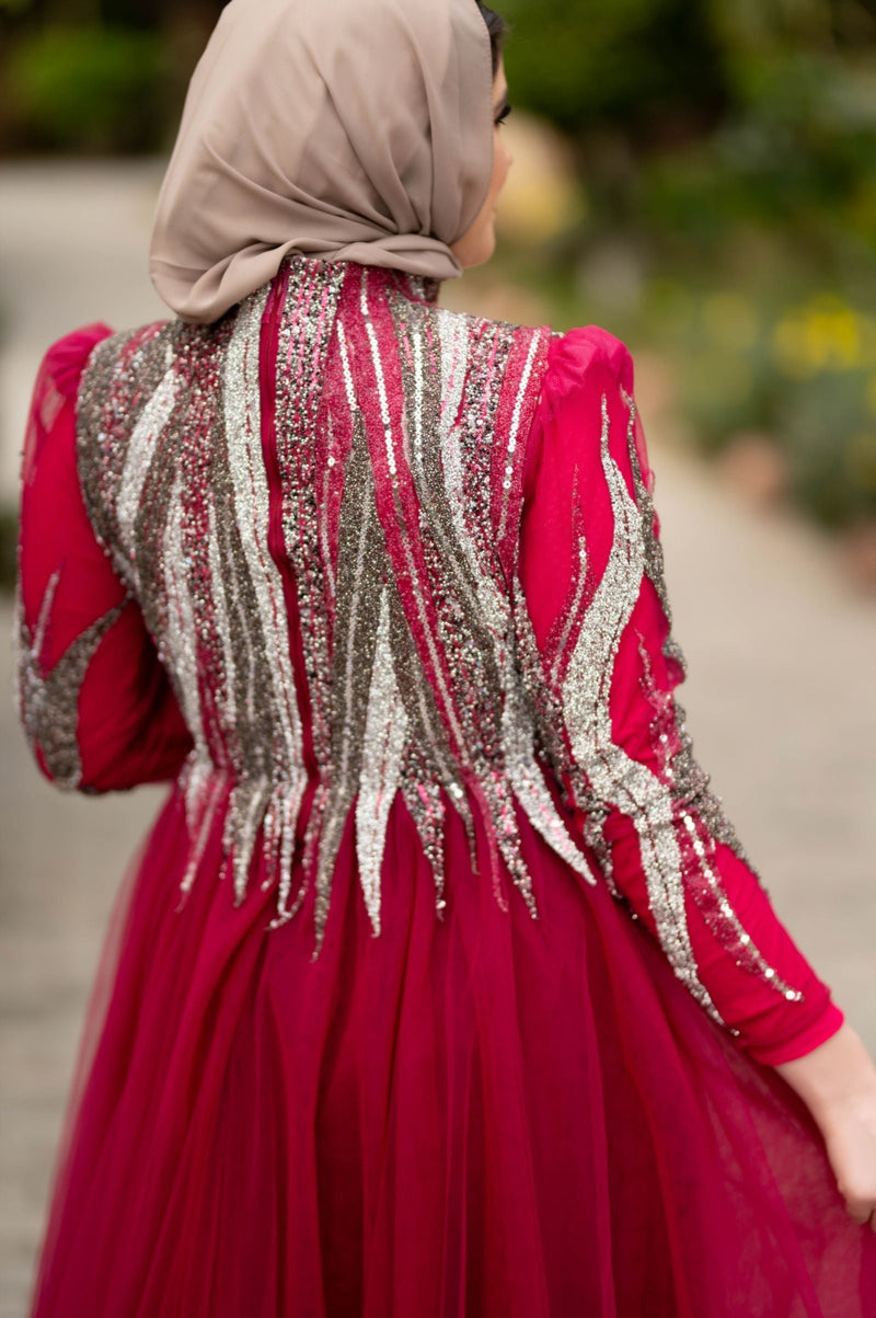 Muslim woman wearing a sparkling red formal gown and hijab outdoors, illustrating red carpet Muslimah, prom and modest evening styling