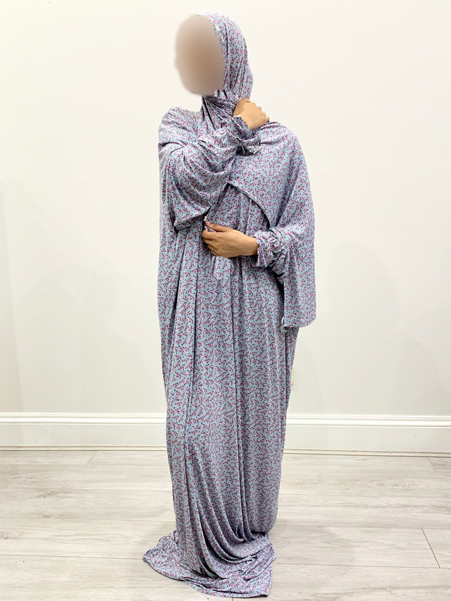 Angled view of Amani’s soft blue floral one-piece prayer dress with attached wrap-around hijab, separate long sleeves and no lace.