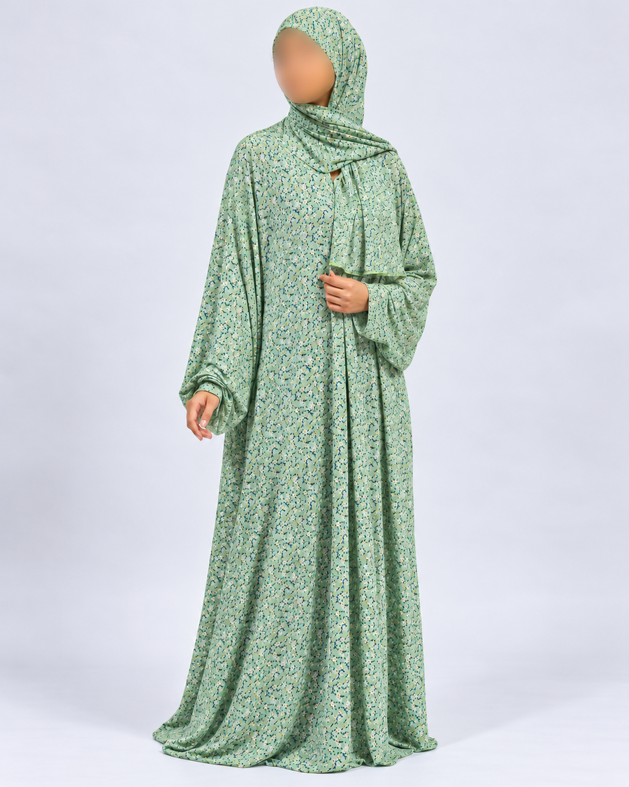 Side-angled view of Amani's soft green one-piece prayer dress, showing the fine blue and yellow floral print and natural sleeves