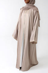 Woman wearing Amani's beige open abaya with satin piping and matching scarf