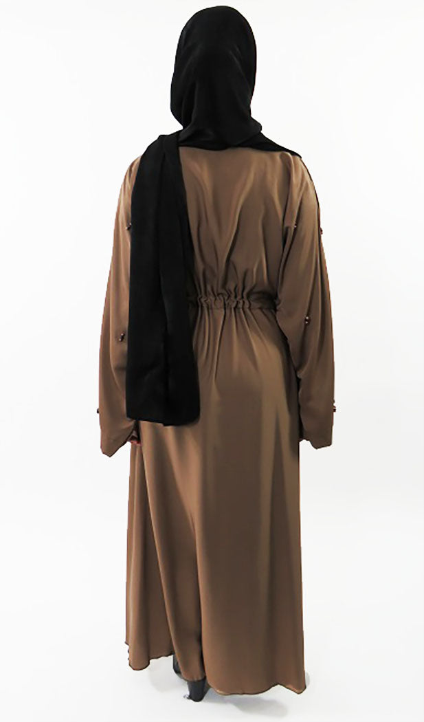 Close-up of hand-embroidered beadwork on light brown abaya