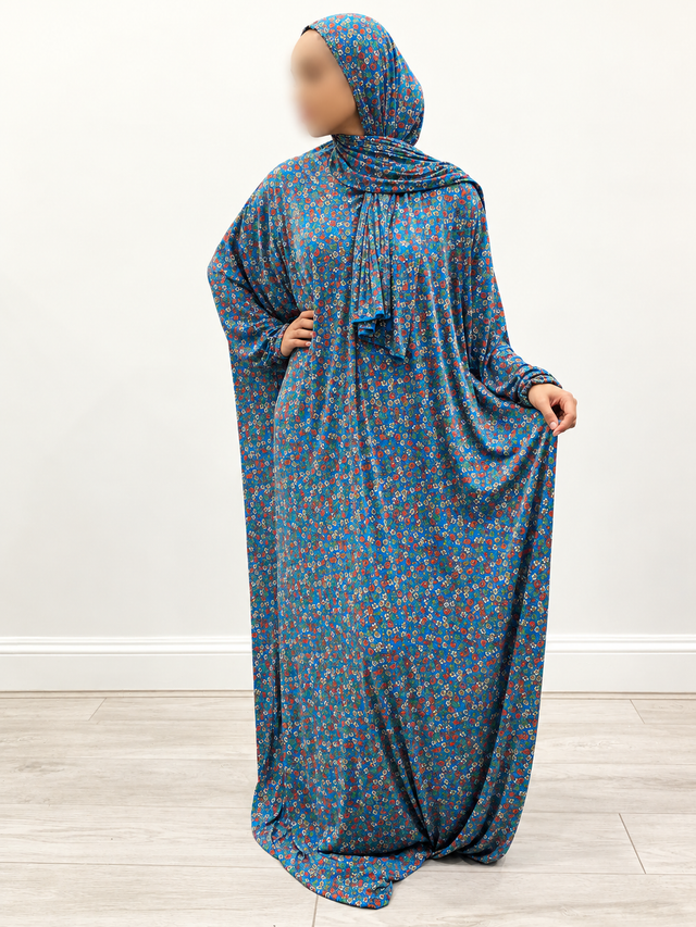 Front three-quarter view of Amani’s blue multicolour floral one-piece prayer dress with attached wrap-around hijab, no lace and gently gathered cuffs