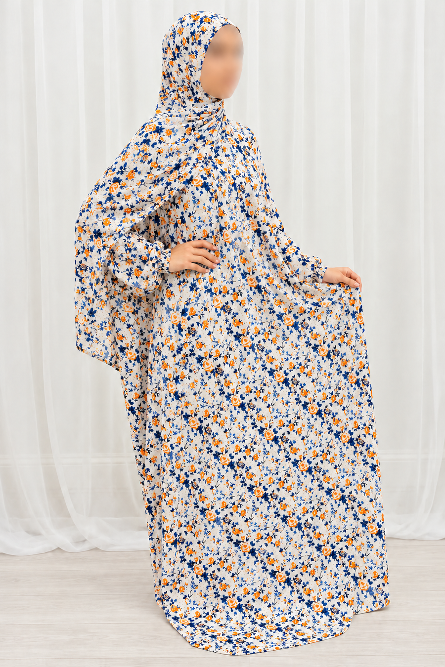 Amani's eggshell white prayer dress with navy leaves and orange flowers, matching attached hijab and hands-together pose, no lace
