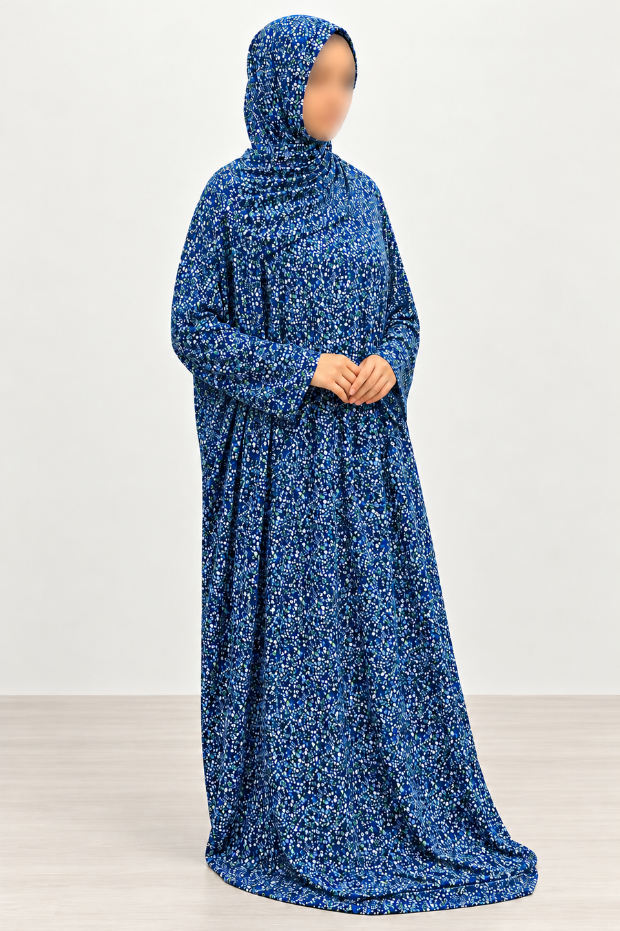 Amani's royal blue micro floral prayer dress and matching attached hijab, hands-clasped pose showing plain straight sleeves and full length