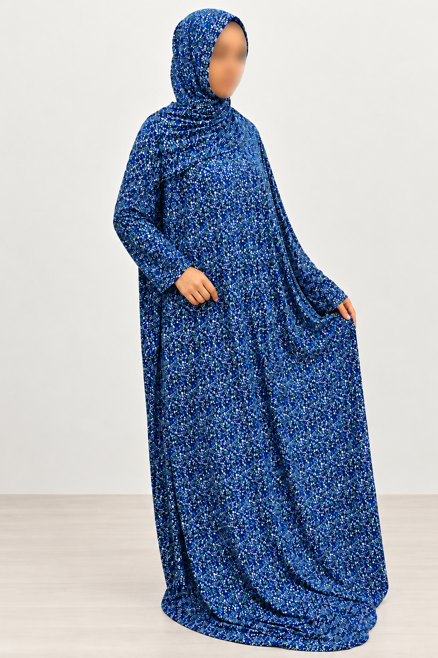 Side-angled view of Amani's royal blue micro floral one-piece prayer dress with attached hijab, loose floor-length drape and plain no-lace cuffs